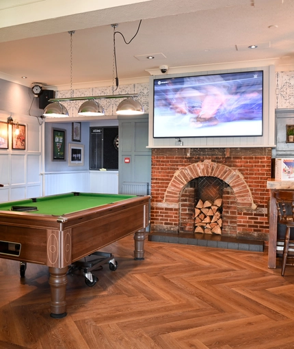 Interior dining area of a pub with a few TVs, a fireplace and a pool table.