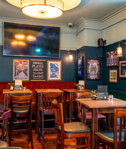 The interior restaurant seating area of the Royal George; with an upholstered booth seat, and a large TV on the wall above it.