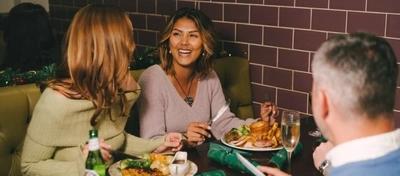 An image of a group of friends sat at a table enjoying Xmas Day main dishes and various drinks within the interior restaurant seating area at a Pub & Carvery venue.