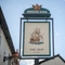 A close up view of the exterior pub sign of The Ship. The sign features an illustration of a large ship sailing on the sea and surrounded by seagulls, above the words "The Ship, Bedford", on a white background.