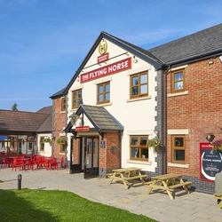 The exterior facade, signage and seating area with tables, chairs and wooden picnic tables, at The Flying Horse in Heald Green.