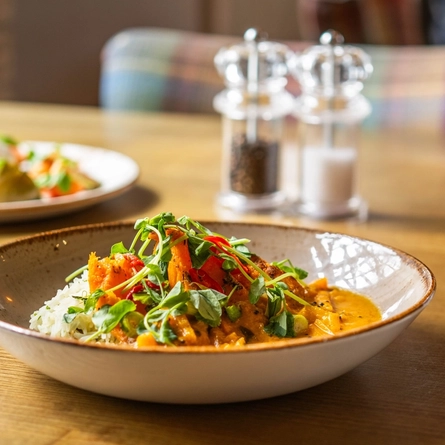 An advertising image of a bowled Malabar Curry dish sat on a table within the interior restaurant seating area at a Chef & Brewer venue.