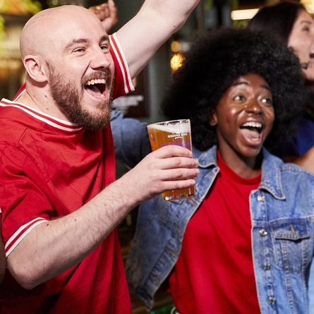 A mixed group of people holding a drink and cheering.