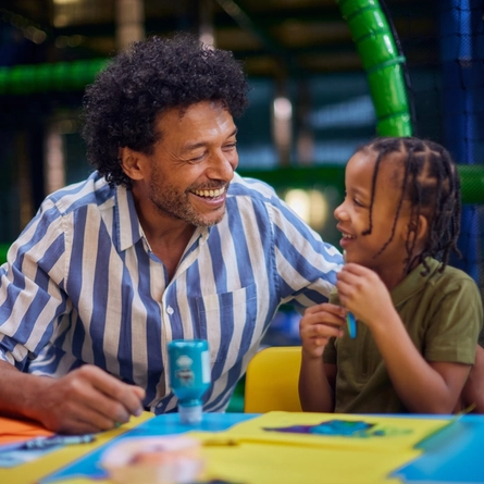 A man participating in crafts with a child at a Wacky Warehouse.