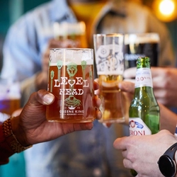 A close up view of a hand holding a glass of Level Head IPA. Other people holding glasses of beer, stout, and a bottle of Peroni 0.0% alcohol beer are visible in the background.