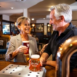An image of 2 people stood at the interior bar with 2 drinks at a Community Pubs With Food venue.