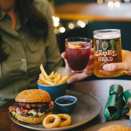 An image of 2 people celebrating with a drinks cheers while enjoying burger dishes within the interior restaurant seating area at an Urban Core venue.