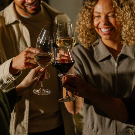 An image of 4 customers enjoying glasses wine and celebrating with a cheers stood within the interior of The Crown.