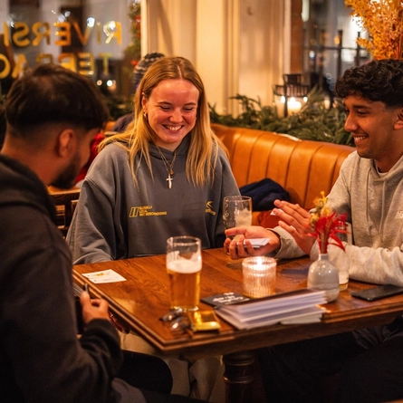 An image of customers sat at tables with drinks playing cards within the interior restaurant seating area of The Crabtree.