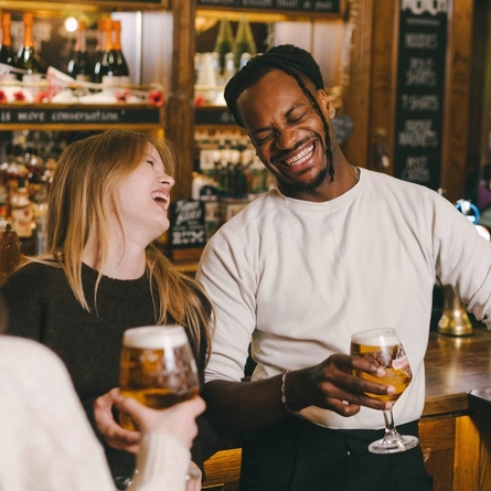 An image of 3 friends stood holding pints of Cruzcampo within the interior bar area at a Greene King venue.