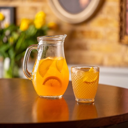 A jug on the table full of Passionfruit Punch Cocktail with a lowball glasses.