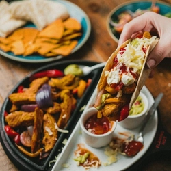 A images of a served portion of fajitas on a skillet and a made up fajita being held by a customers hand, served at Flaming Grill venues.