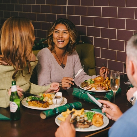 An image of a group of friends sat at a table enjoying Xmas Day main dishes and various drinks within the interior restaurant seating area at a Pub & Carvery venue.