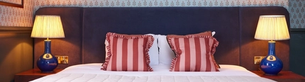 A double bed, cushions and lamps in one of the hotel rooms at The Dog and Partridge.