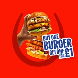 Promotional graphic reading “Buy One Burger, Get One for £1” alongside two crispy chicken burgers held in hands, topped with cheese, lettuce, red onion and sauce, on a red background with a horseshoe graphic. with cheese