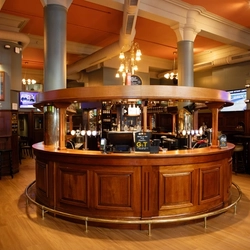 The wood panelled interior restaurant seating area and U-shaped bar at the Rhoderick Dhu in Glasgow; with upholstered booth seating, and TVs on the walls.
