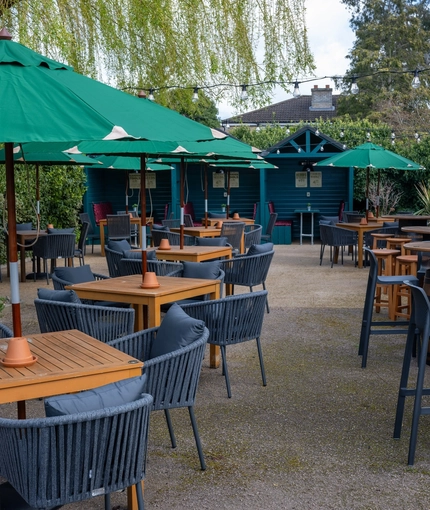 The exterior beer garden seating area of the Golden Hind in Cambridge, with shade umbrellas, string lights, and under cover seating areas.