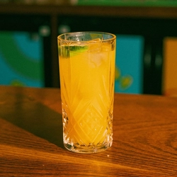 A close up view of a Pina Colada cocktail served in a highball glass with ice and a lime wedge. The glass stands on the bar inside a pub.