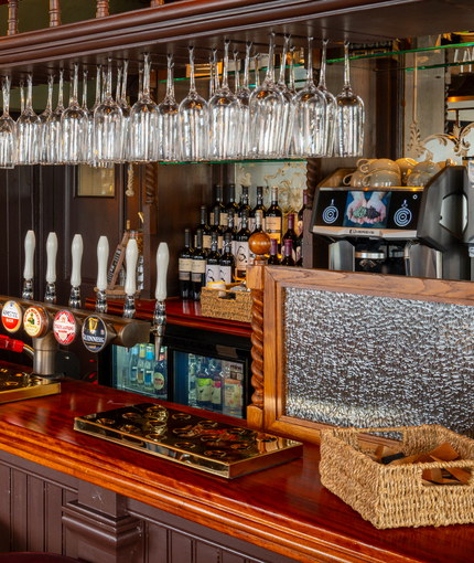 The wood panelled bar inside The London Apprentice in Isleworth, with bar stool seating, golden drinks trays on the counter, and glasses hanging in racks above it.