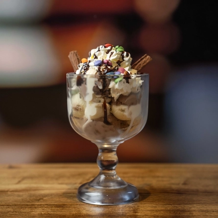 A Candy Mania dessert in a sundae glass on a wooden table.