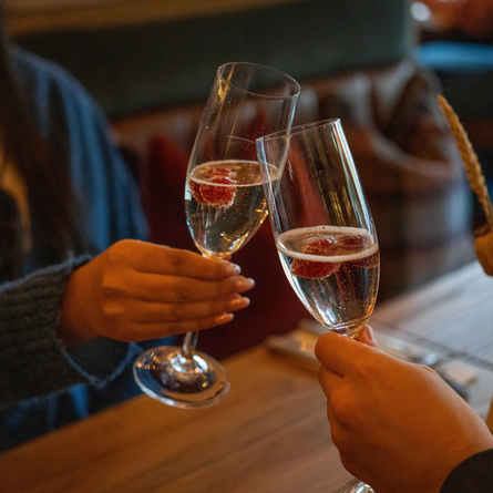 A close up view of two people at a restaurant table, clinking together glasses of Prosecco garnished with berries.