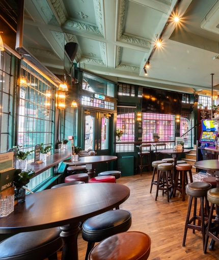 The bar and interior restaurant seating area at The Golden Lion in Soho, with a TV on the wall, a gaming machine, and glasses hanging in racks above the counter.