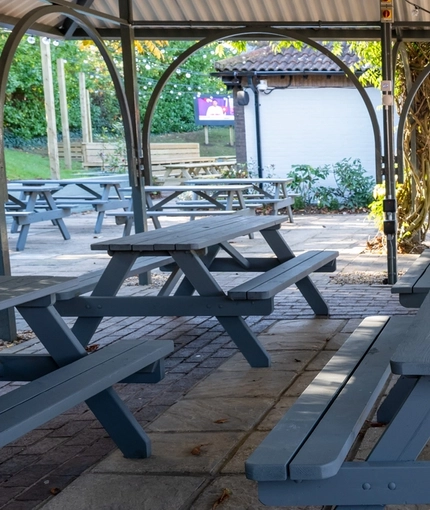 The exterior undercover beer garden seating area at the Clocktower in Milton Keynes, with wooden picnic tables.