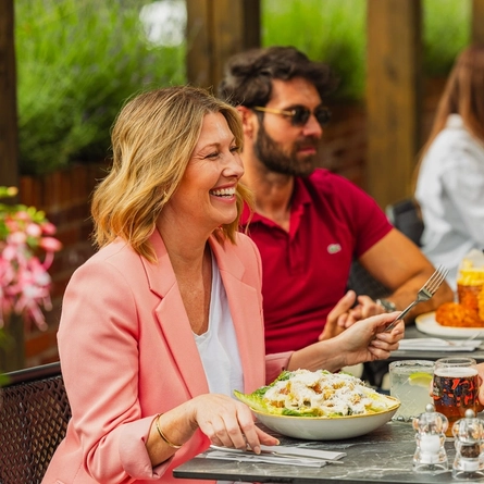 A group of people enjoying various dishes from the mains menu and drinks within the exterior beer garden seating area at a Crafted venue.