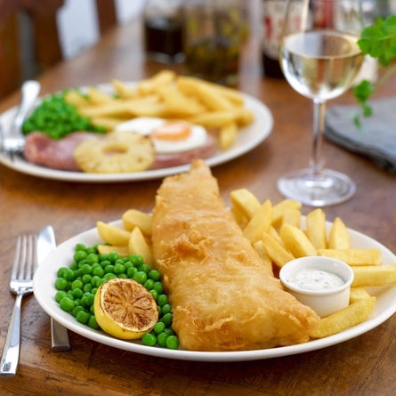 A plate of fish and chips and a plate of gammon and chips
