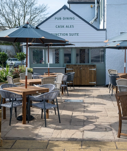 The paved exterior beer garden seating area at The Blue Cap in Sandiway, with wooden tables, planter boxes, and shade umbrellas.
