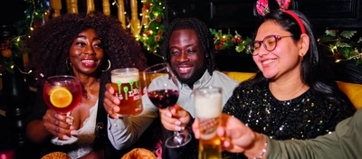 A group of people celebrating a festive Cheers while enjoying various main meals and drinks within the interior restaurant and seating area of Greene King Pub venue.