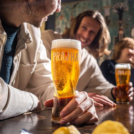 An image focusing on a pint of Pravha with a group of people in the background.