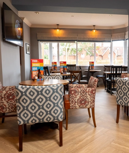 An interior restaurant seating area at The Heron; with wooden flooring, upholstered chairs, and a TV on the wall.