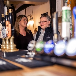 A Woman and Man stood behind the bar smiling