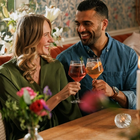 An image focusing on 2 customers enjoying Valentines Day Date Night cocktails and celebrating with a cheers sat at a table within the interior seating area at The Crown.