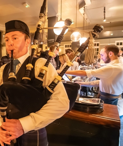 An image of people being entertained by a Bagpipe Player within the interior of the venue during a Burns Night Event at The Crabtree.