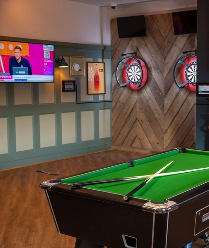 The interior games area at the Green Posts in Portsmouth, with two dartboards, a pool table, a fireplace, and two TVs on the walls.