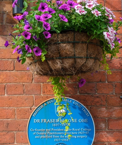 An image of the exterior hanging basket decor and historic information plaque at The Guild.