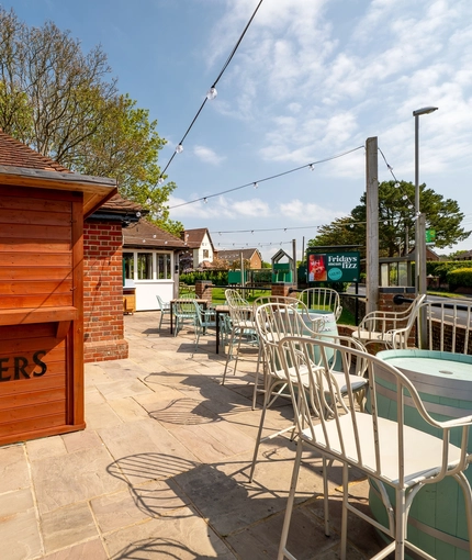 A paved seating area at The Walkford, with beer barrel tables, and string lights overhead.
