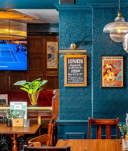 An interior restaurant seating area at The Earls Court Tavern, with TVs and framed artwork on the walls.