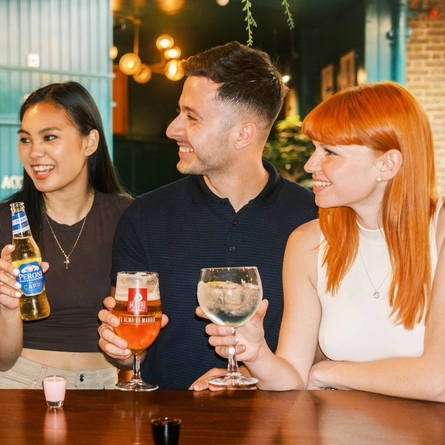 A group of people around a table with drinks in their hands and on the table.