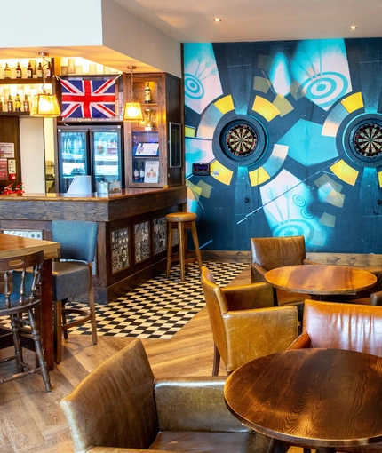 Interior dining area of a pub with a bar, a fireplace, and a few dartboards.