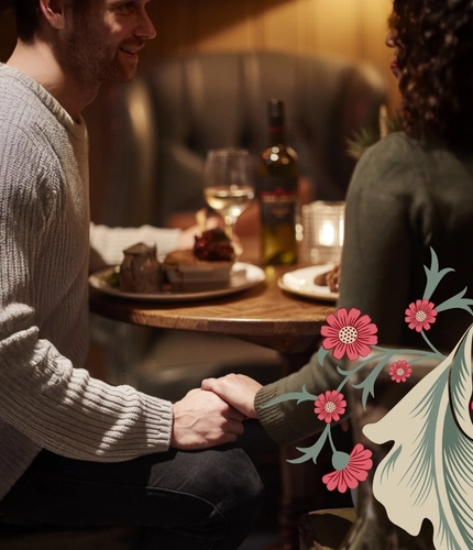 A couple at a dark wood table holding hands. The image is taken from behind and it is cut off at the shoulders.