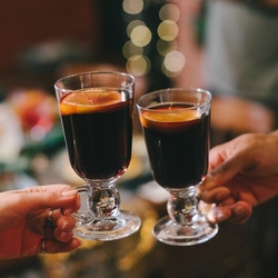 Two hands holding a glass of mulled wine in mulled wine/irish coffee glasses.