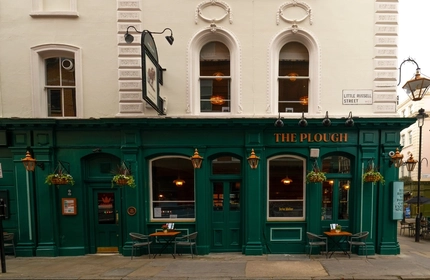 The exterior facade, signage, and seating area at The Plough in Bloomsbury, with flower baskets hanging from the walls.