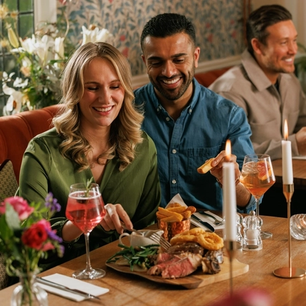 An image focusing on 2 customers enjoying a Valentines Day Ribeye Steak boarded dish sat at a table within the interior restaurant seating area of The Crown.