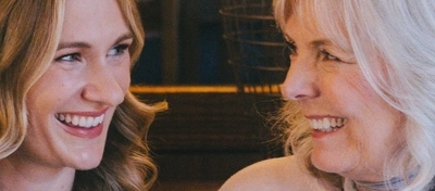 Four people sitting at a restaurant table with plates of food in front of them. One person is holding a cocktail, and another person is holding a glass of wine.