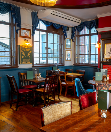 An interior restaurant seating area at the Two Chairmen in St James's, with wooden flooring, framed artwork on the walls, and a fireplace.