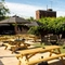 The exterior beer garden seating area at The Bramford Arms in Woodsetton, with paved and grass areas, wooden picnic tables, shade umbrellas, and string lights.