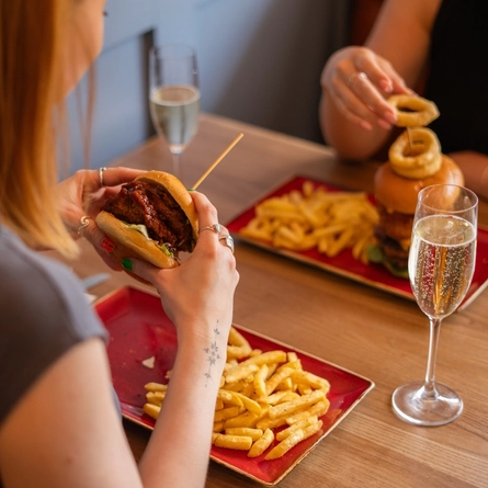 A lifestyle image of a group of people enjoying a glass of Sparkling Wine with a burger, seated at an indoor table.